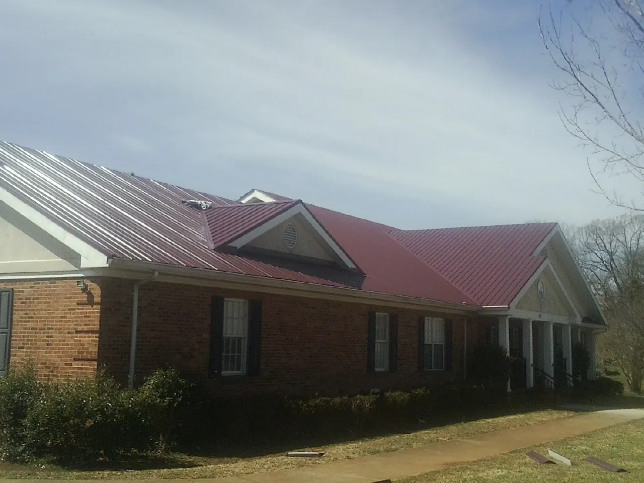 Red metal roof with gabled entries on a long brick building, from a Hail Damage Roof Repair job in Delmar