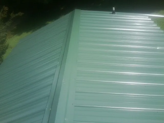 New green metal panels meeting at the ridge of a roof — Flat Roof Repair work by our crew in Delmar