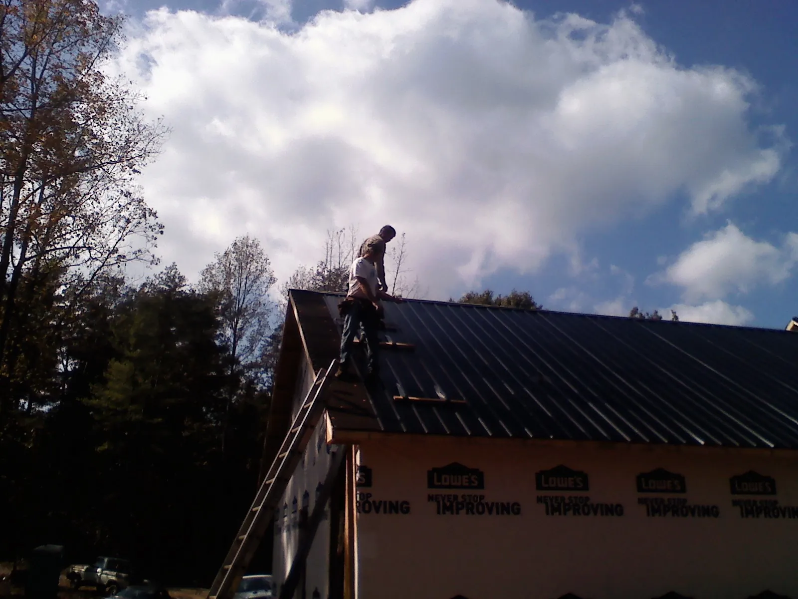 Roofer fastening dark metal panels high against a cloudy sky, from a Roof Inspection job in Delmar