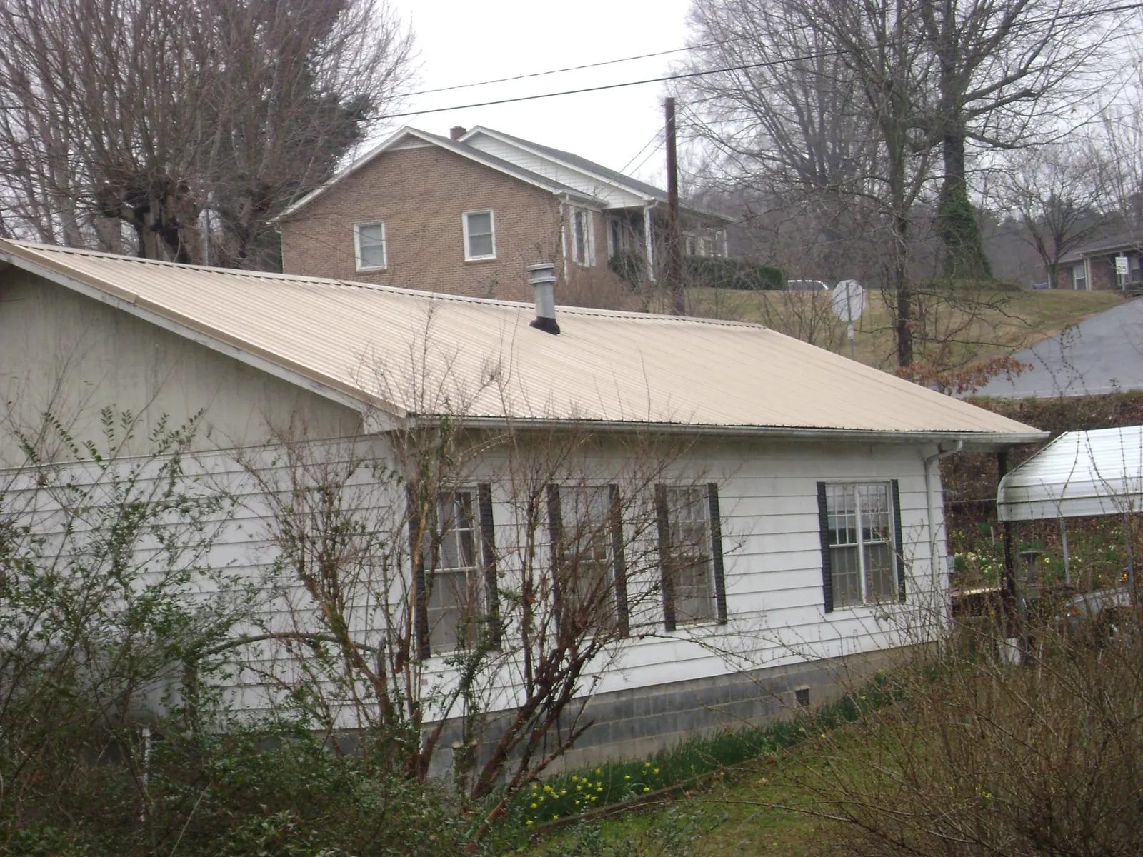 Tan metal roof on a white sided house set into a hillside — Commercial Roofing by Roofing Brothers in Delmar